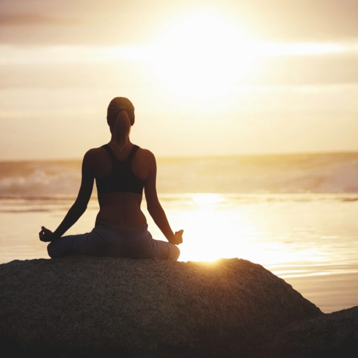 Silhouette image of a woman practicing yoga in lotus position by the sea on a rock